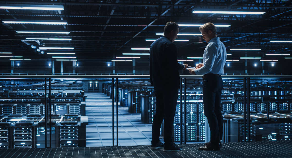 Two business professionals standing on an elevated platform in a large data center, engaged in discussion.