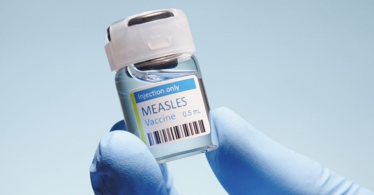 Healthcare worker in blue gloves holding a measles vaccine vial